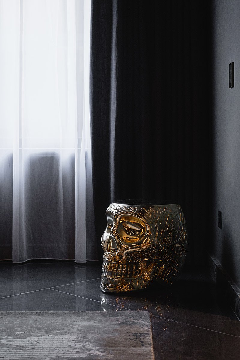 Gold skull side table in a dark curtained MAD Studio interior